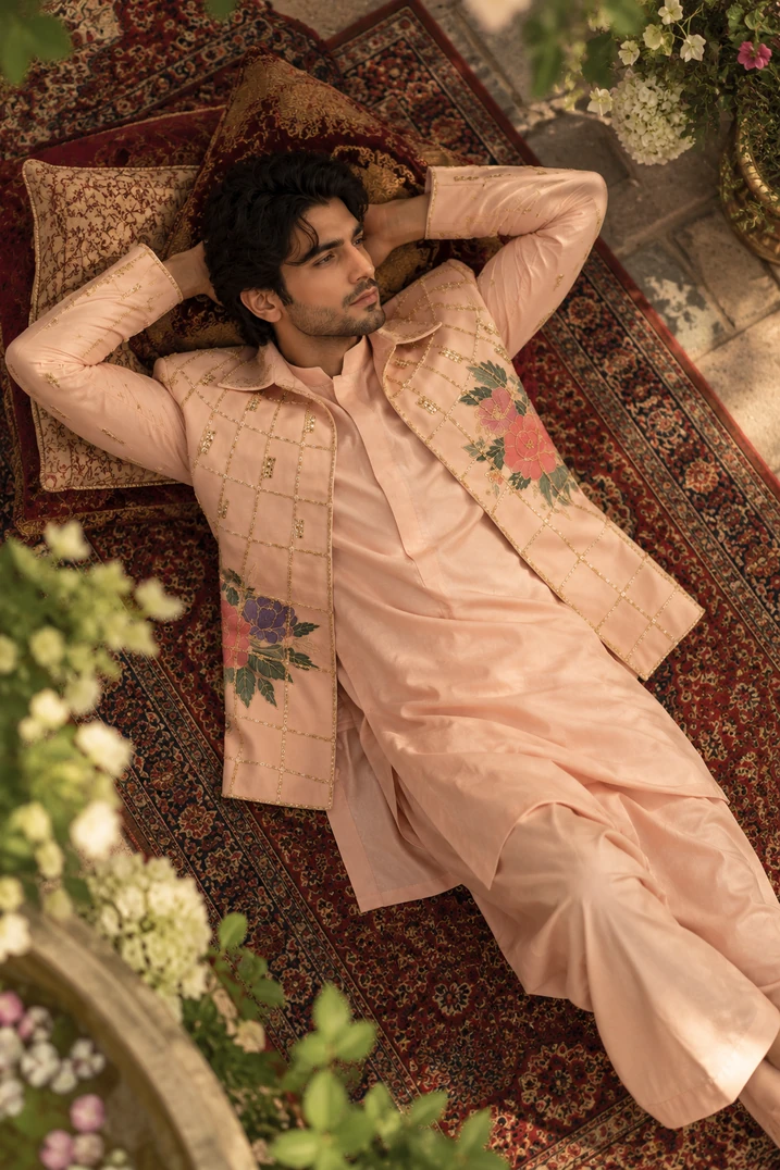 A model wearing a blush embroidered sherwani lying on carpet